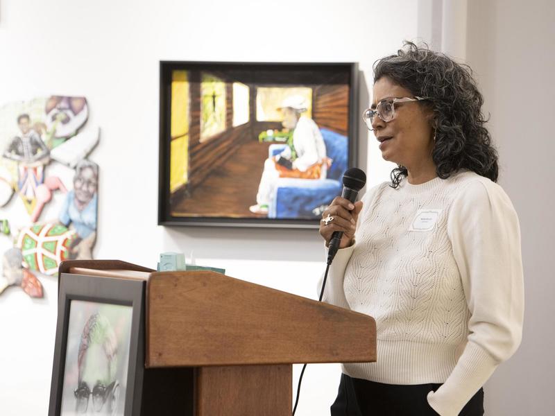 Photo of Rachel Bryant holding a microphone at a podium and speaking about the Center for Black and Indigenous Praxis