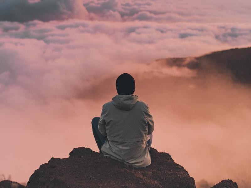 Person sitting on a mountain looking into the sky